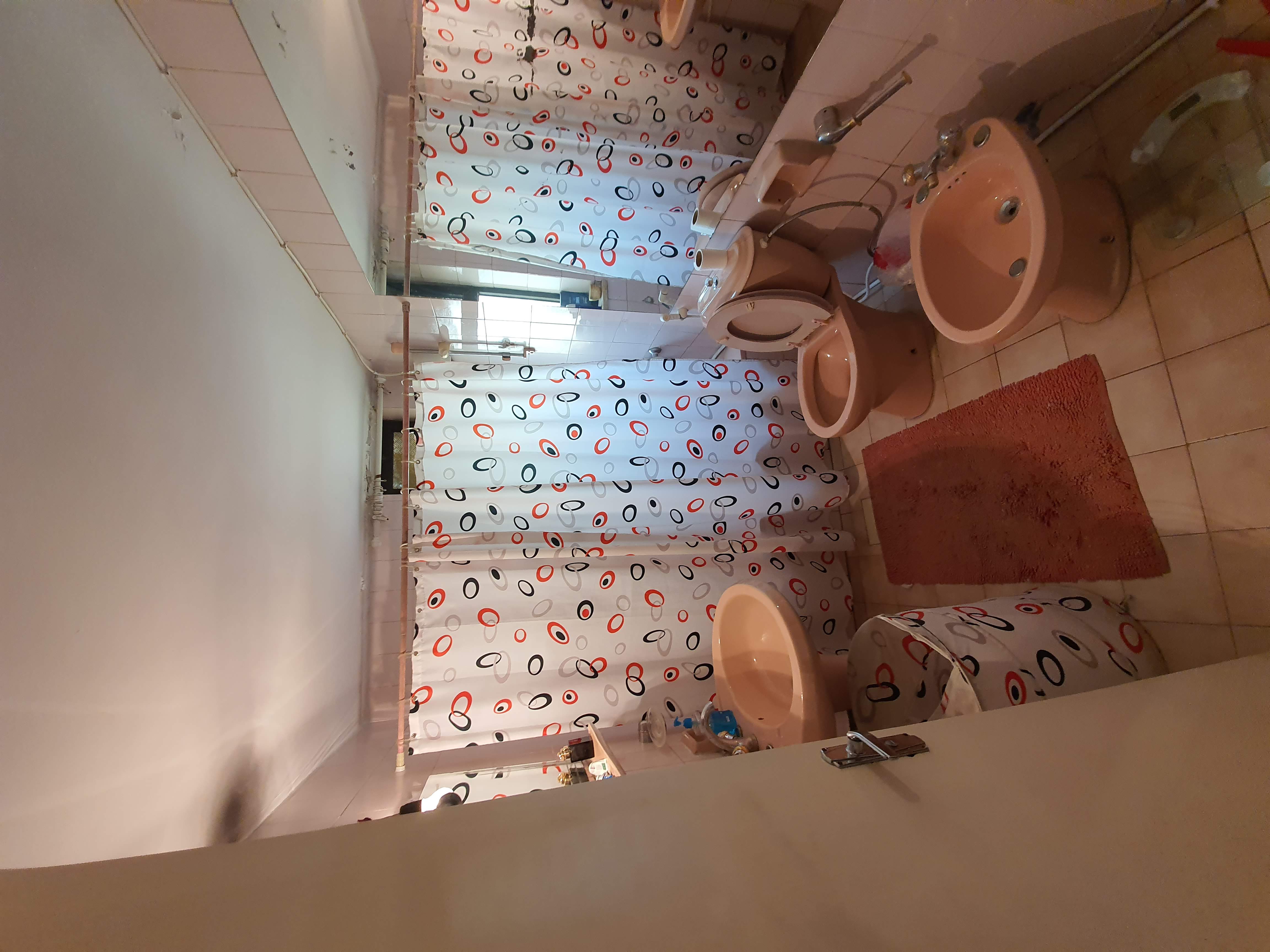 Bathroom before renovation — dated pink suite and shower curtain