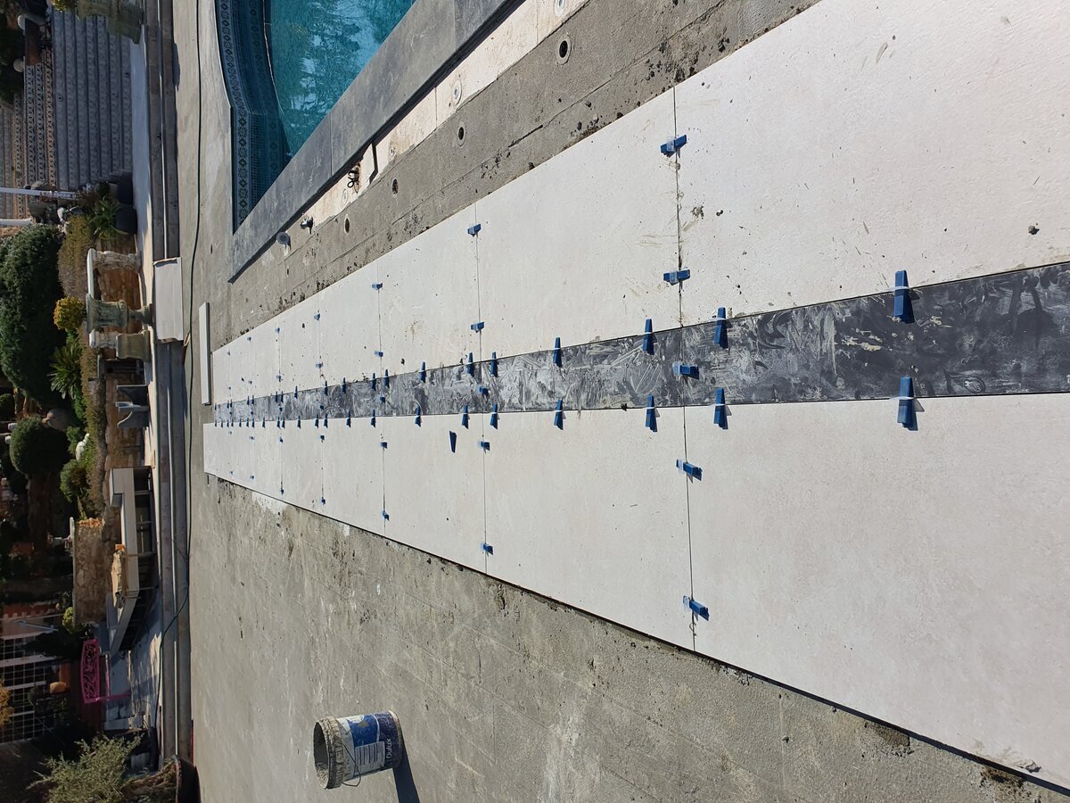 Pool terrace — large-format stone tiles being laid with levelling clips alongside the pool edge