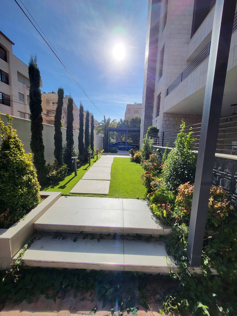 Landscaped garden by day — cypress trees and paved walkway